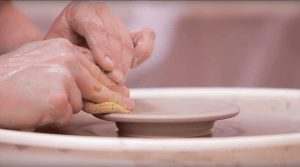 Hands sculpting soft clay on a pottery wheel